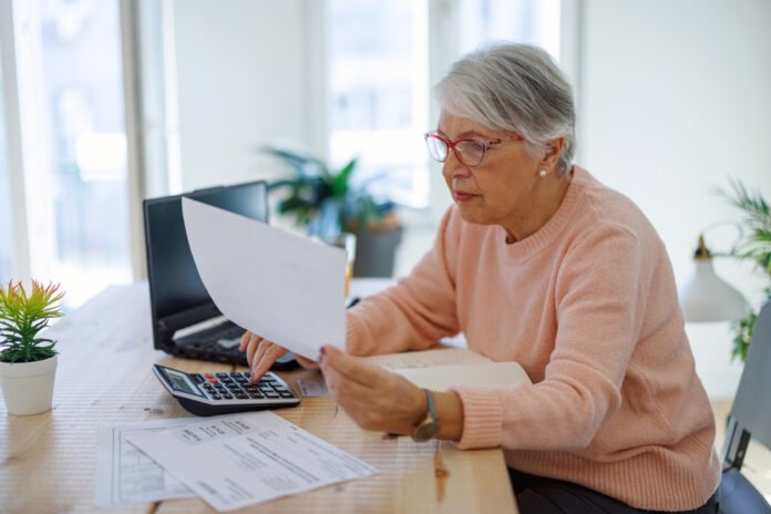 Pensive aged woman using laptop paying bills online at home. Senior businesswoman work on computer.